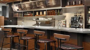 A bar area with a long counter, stools, and a menu board. - Courtyard by Marriott Atlanta Perimeter Center (Atlanta)