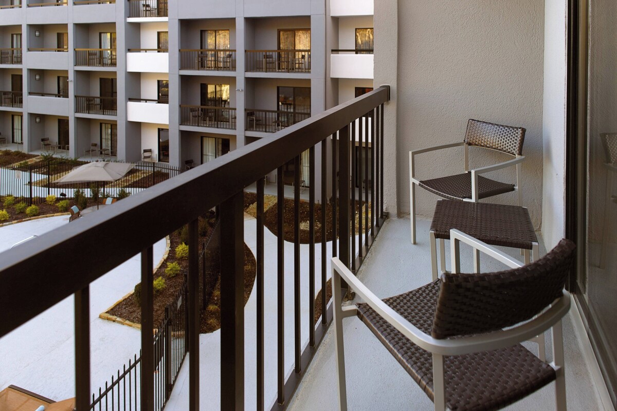 A balcony with a view of a courtyard and a pool, furnished with a table and two chairs.