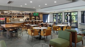A modern restaurant with multiple seating areas, including round tables and cushioned chairs. - Courtyard by Marriott Atlanta Perimeter Center (Atlanta)