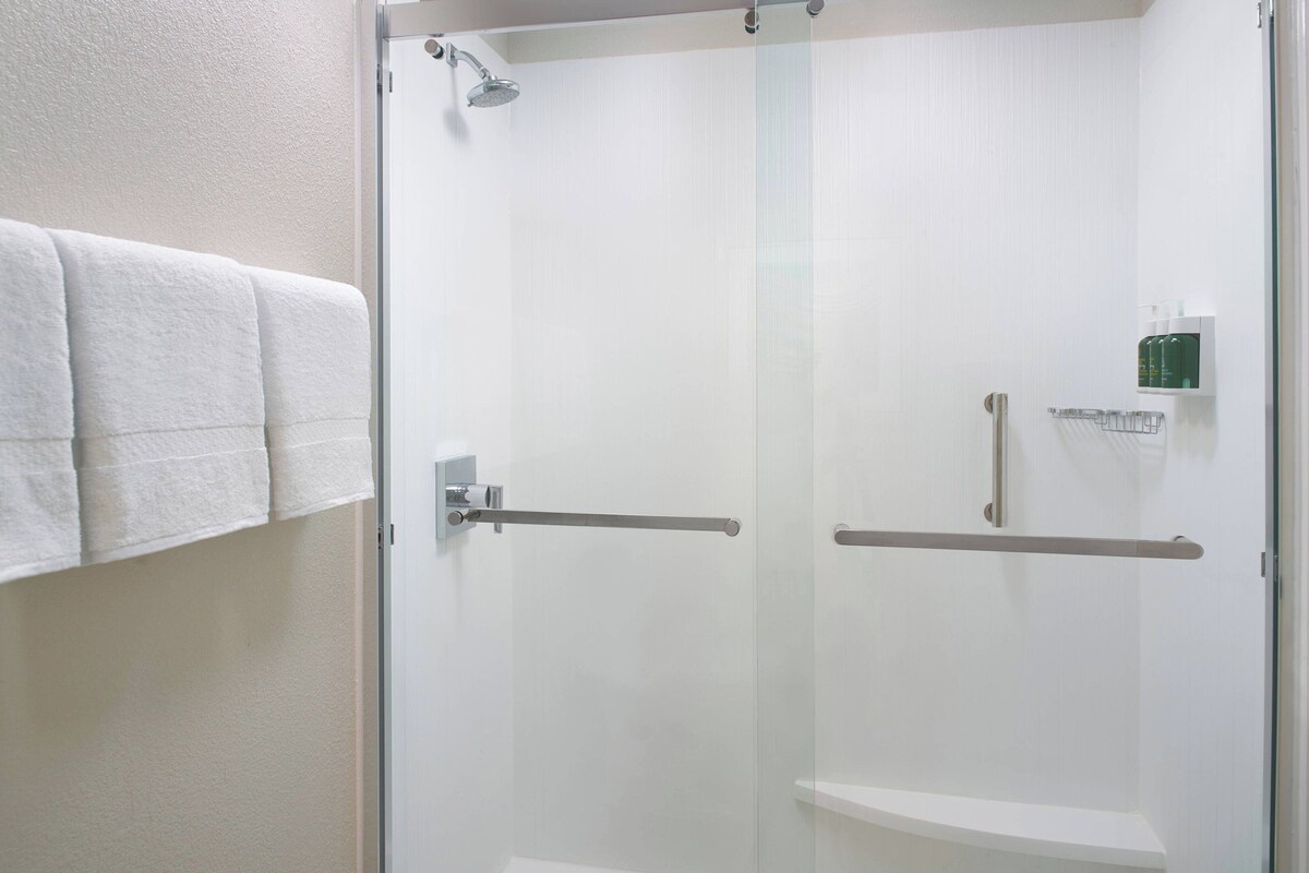 A glass-enclosed shower with a towel rack and a small shelf with toiletries.