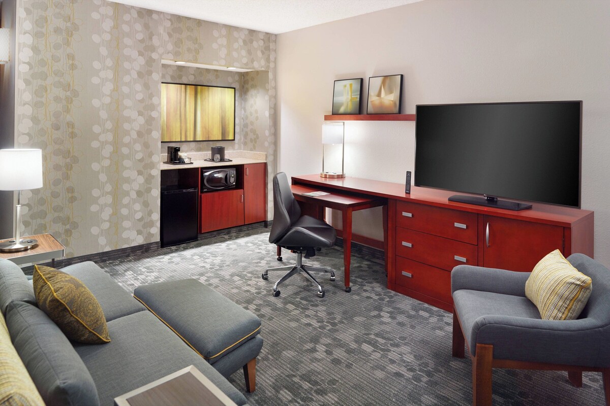 Une chambre d’hôtel équipée d’un canapé, d’un fauteuil, d’un bureau avec une télévision, d’un four à micro-ondes et d’une petite kitchenette.