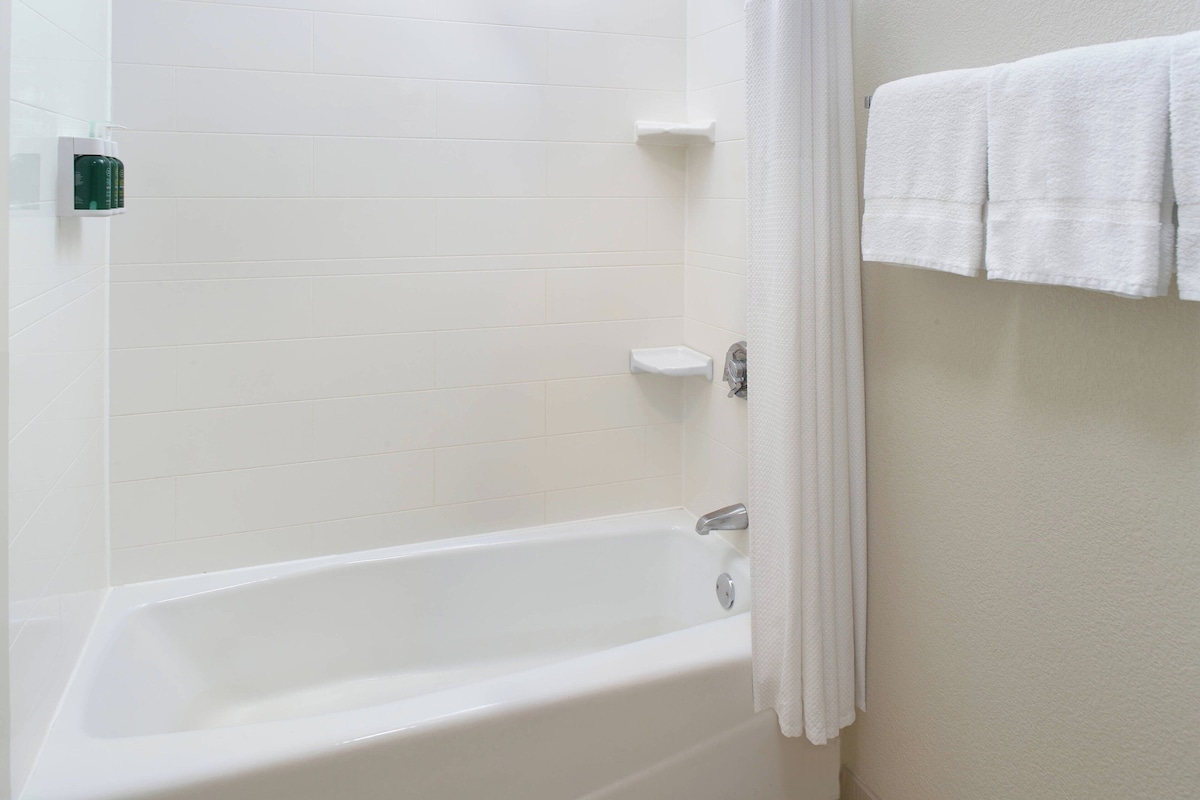 A white bathtub with a shower curtain, a small shelf, and a towel rack with towels.