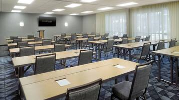 A conference room with multiple tables and chairs, a podium, and a large screen on the wall.