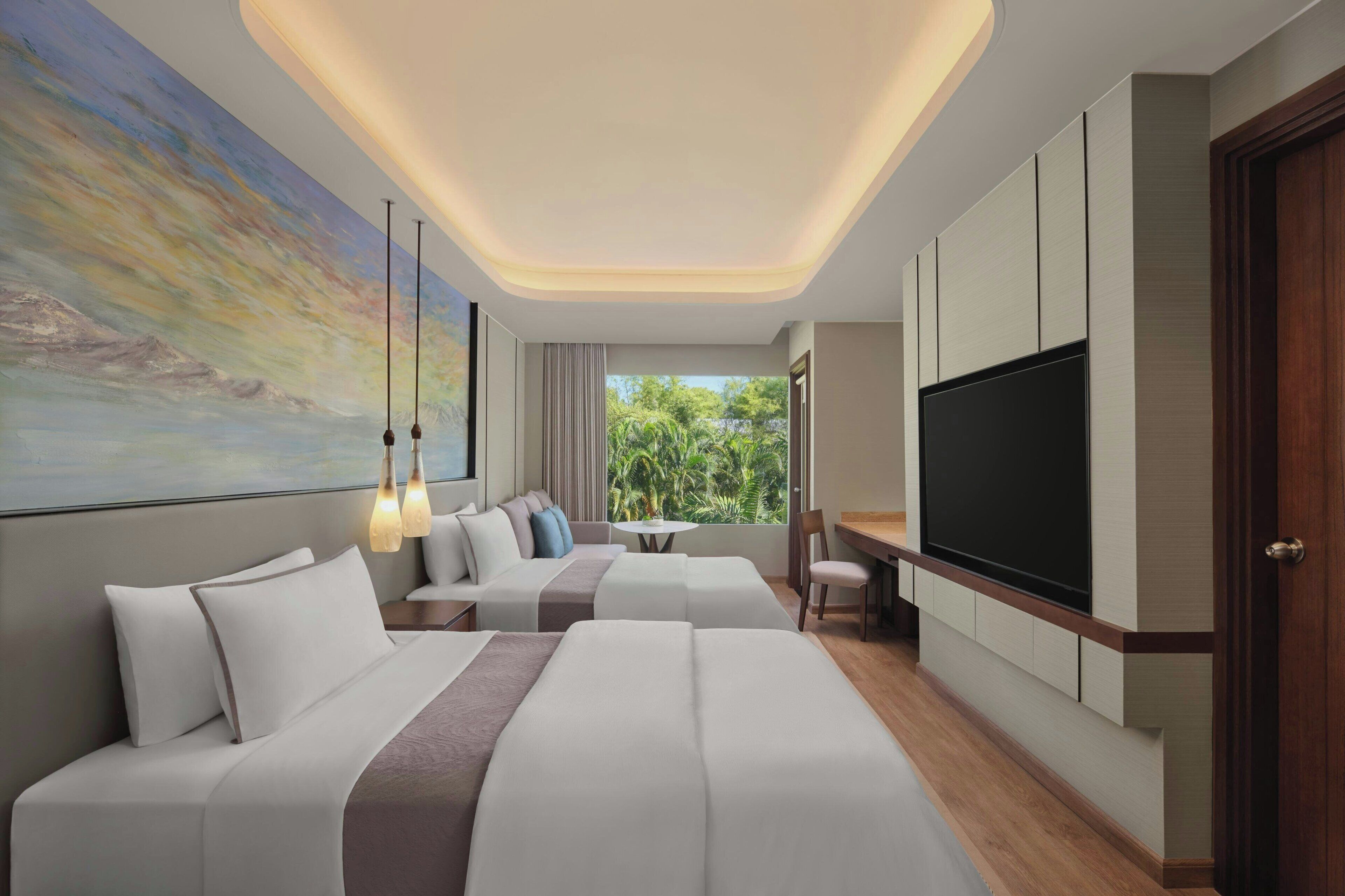 A modern hotel room with a large bed, a sofa, a desk, and a TV.