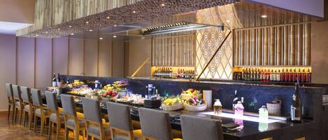A restaurant with a long counter, multiple chairs, and a variety of food and drink items displayed.