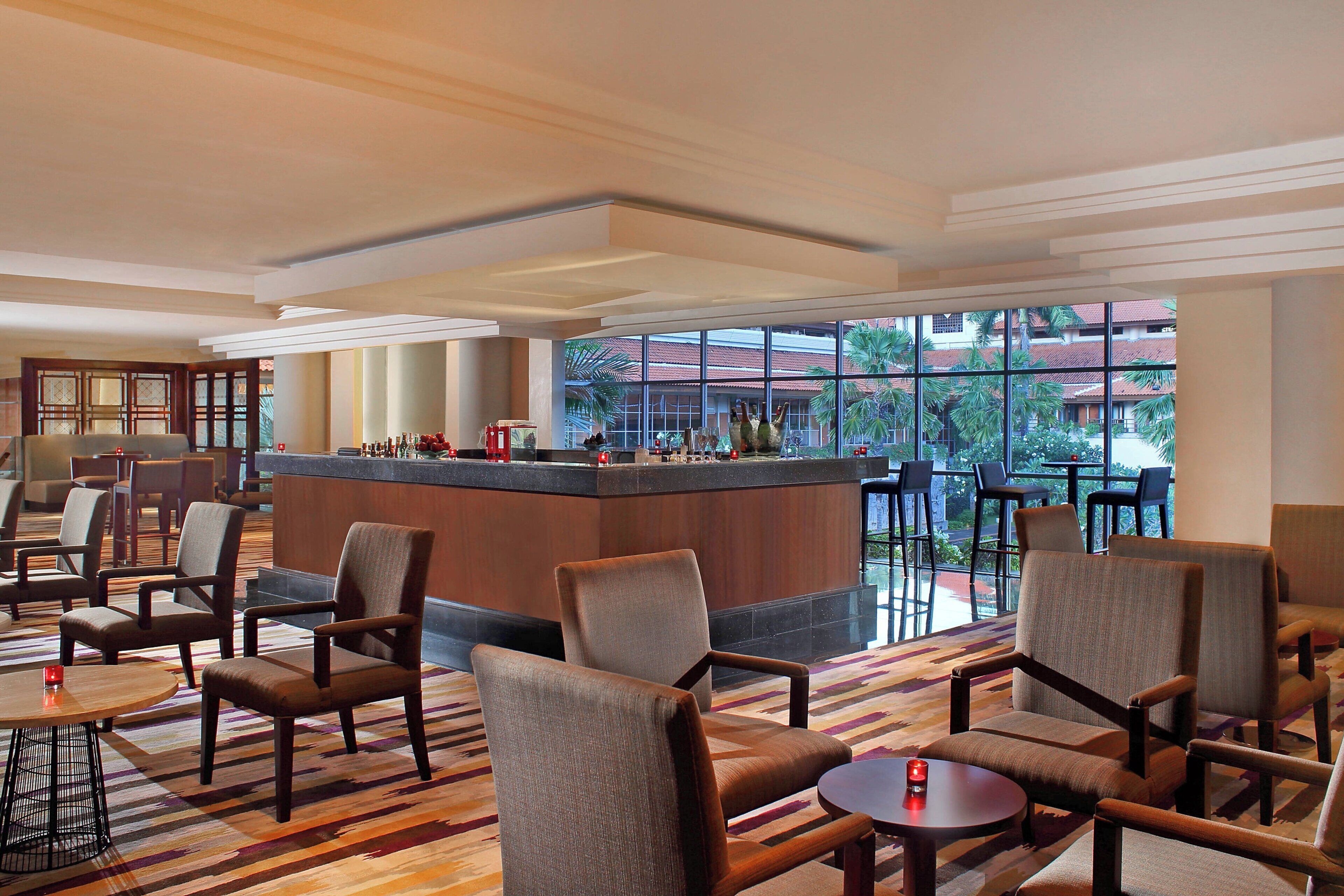 A hotel lobby with a bar area, seating arrangements, and large windows offering views of palm trees and buildings.
