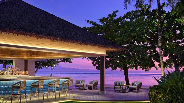 An outdoor bar area with seating, a thatched roof, and a view of the ocean at dusk. - The Westin Resort Nusa Dua, Bali (Nusa Dua)