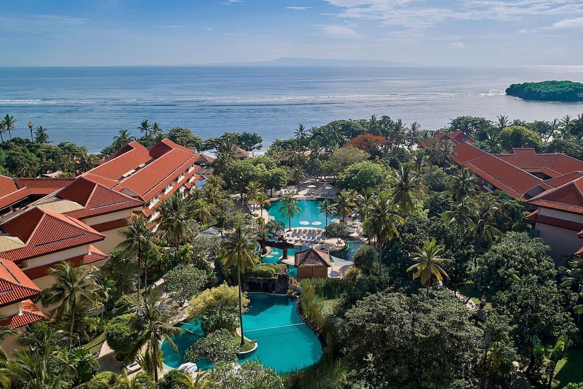 A resort with multiple buildings, a central swimming pool, and a view of the ocean.
