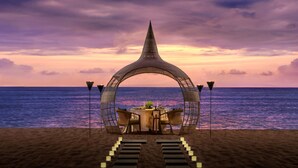 A beachside dining setup with a table and chairs under a unique arch structure, overlooking the sea. - The Westin Resort Nusa Dua, Bali (Nusa Dua)