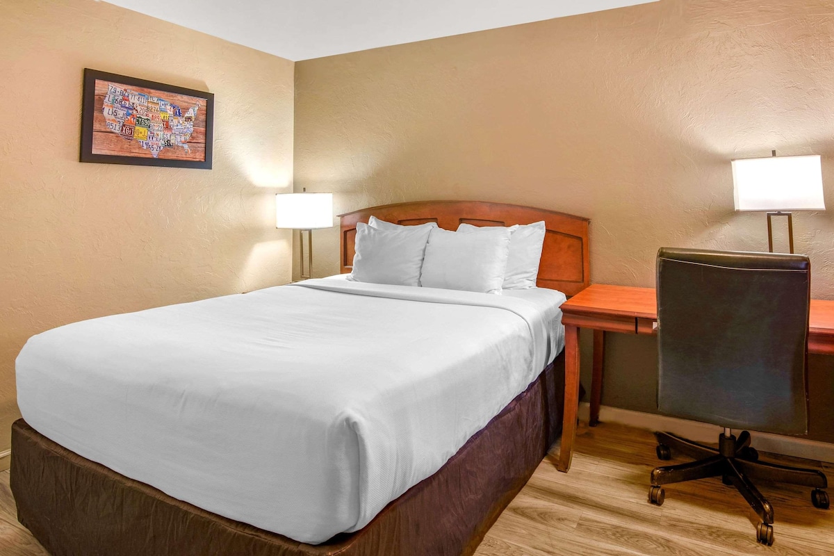 A hotel room with a bed, two bedside lamps, a desk, and a chair.