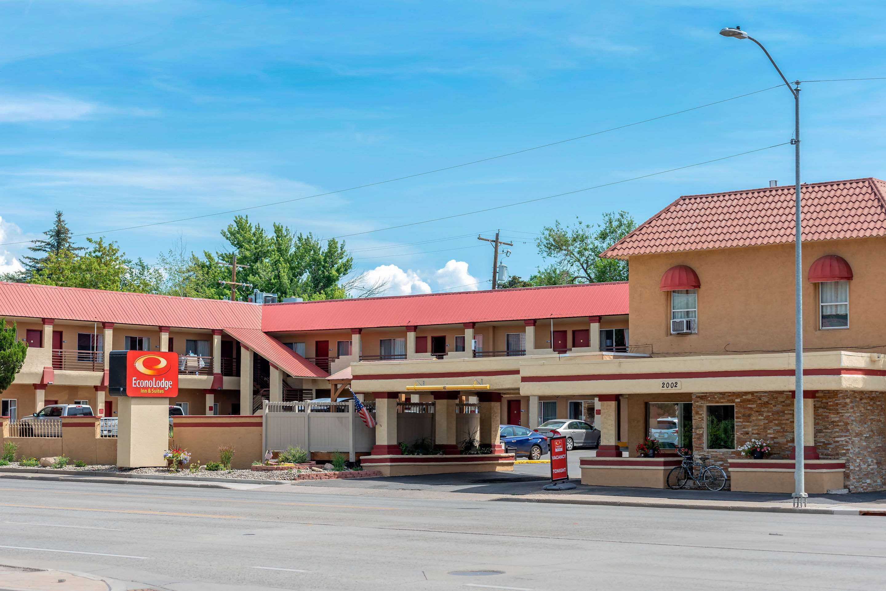 Un motel amb teulada vermella, un rètol de EconoLodge Inn & Suites i un aparcament amb cotxes i una bicicleta.