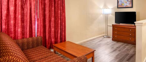 Una sala de estar con un sofá, una mesa de centro de madera, un televisor, una lámpara y un aparador.