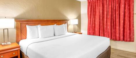 Una habitación de hotel con una cama grande, dos mesitas de noche con lámparas y una cortina roja.