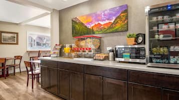A modern kitchen with a coffee station, wooden chairs, and a painting of mountains.