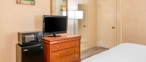 A hotel room with a bed, a wooden dresser with a television and a microwave, a door, and a sign on the wall.