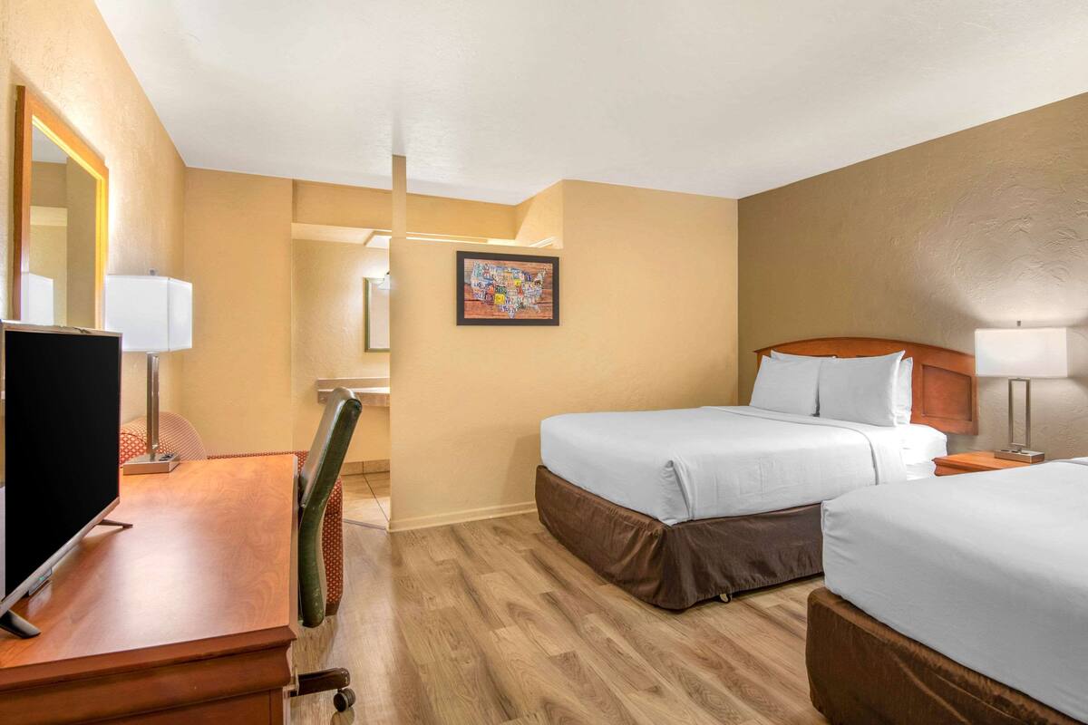 A hotel room with two beds, a desk with a TV, and a mirror.