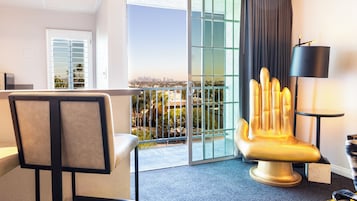 A hotel room with a balcony, a chair, a lamp, and a view of the city skyline.