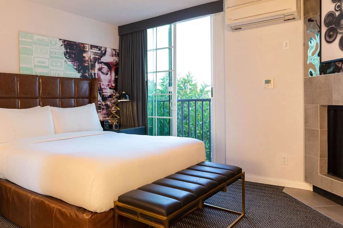 A hotel room with a large bed, a bench, a fireplace, and a balcony with a view.