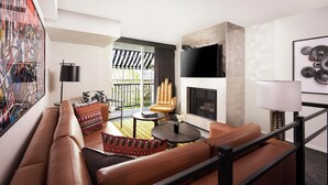 A modern living room with a leather sofa, a round coffee table, and a fireplace. There is a large window with a view of the outdoors.