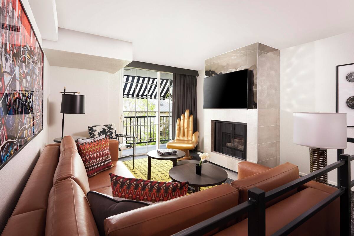A modern living room with a leather sofa, a round coffee table, and a fireplace. There is a large window with a view of the outdoors.