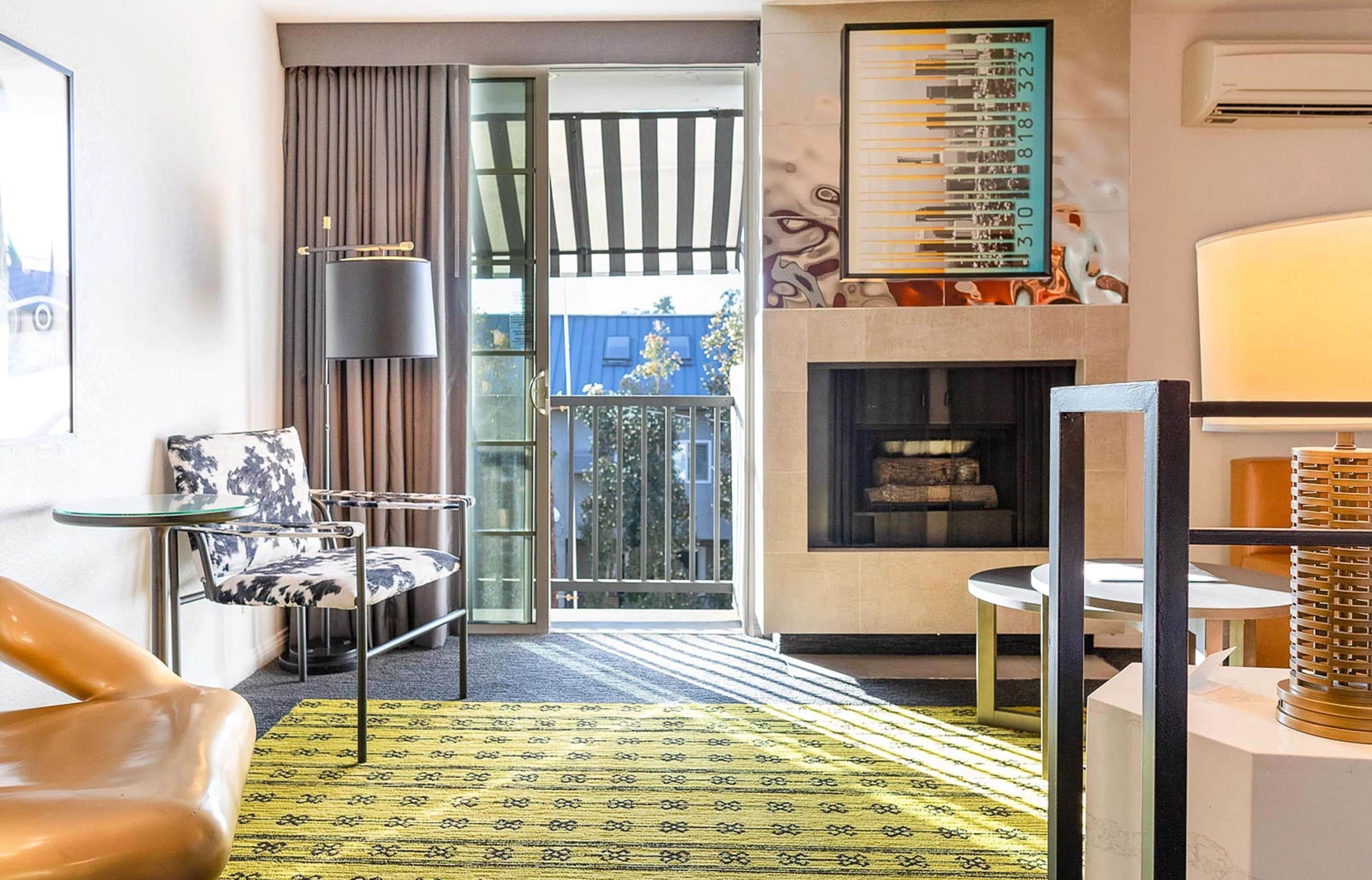 Une chambre d’hôtel moderne dotée d’une porte vitrée donnant sur un balcon, d’une cheminée et d’un tapis à motifs.