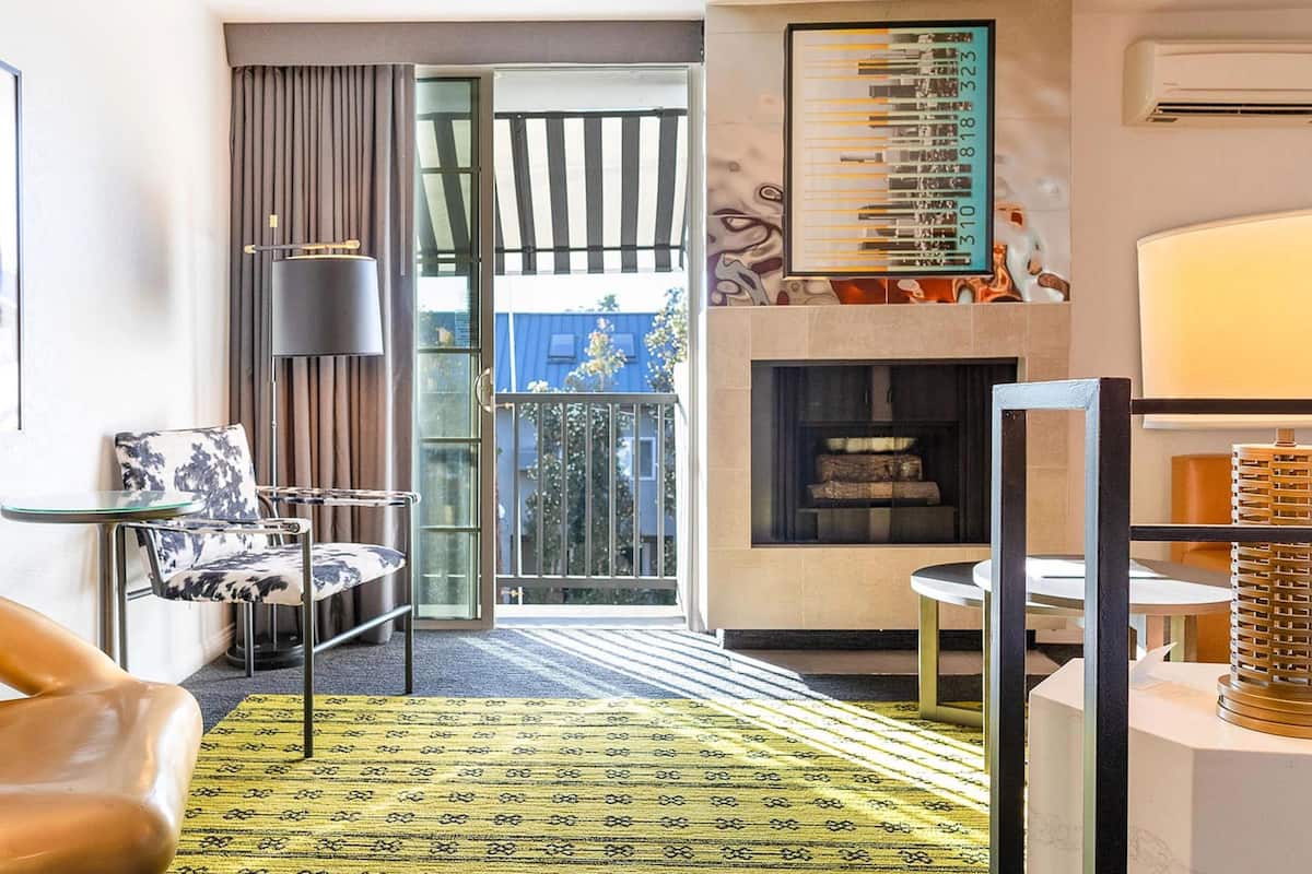 A modern hotel room with a glass door leading to a balcony, a fireplace, and a patterned rug.