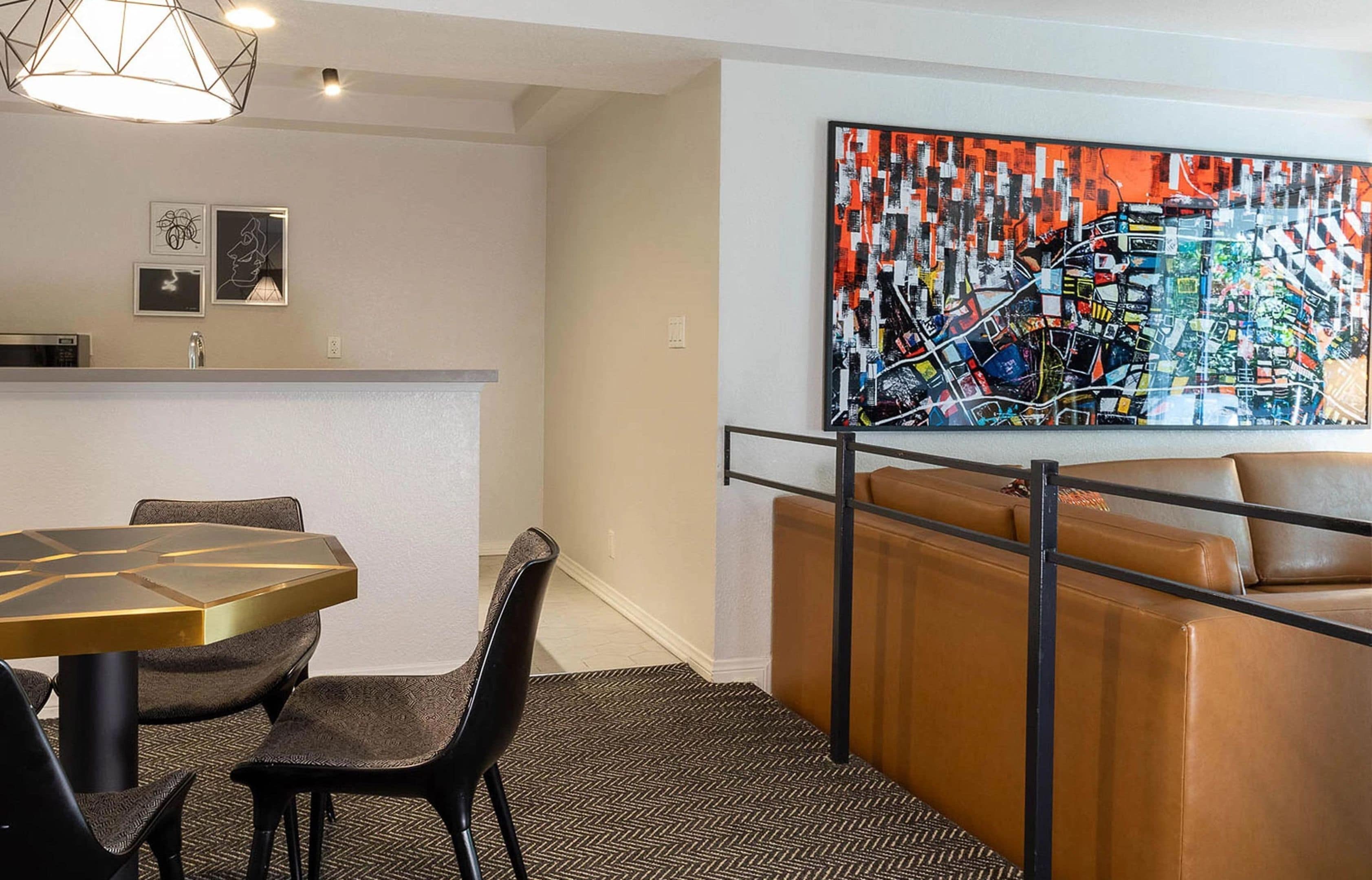 A modern hotel room with a dining area, a sofa, and a large abstract painting on the wall.