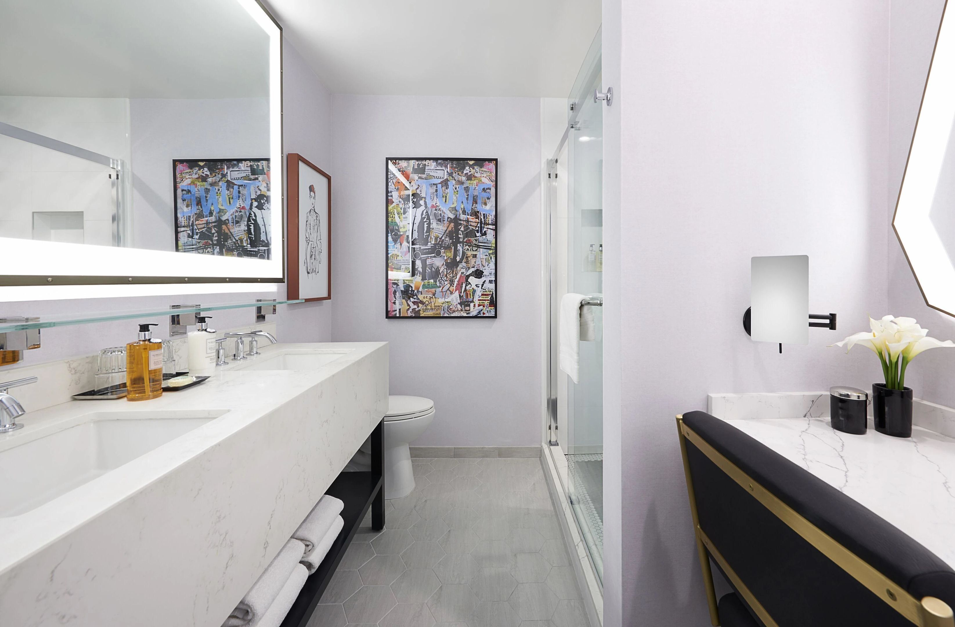 A modern bathroom with a glass shower enclosure, a white sink with a marble countertop, and two framed artworks on the wall.