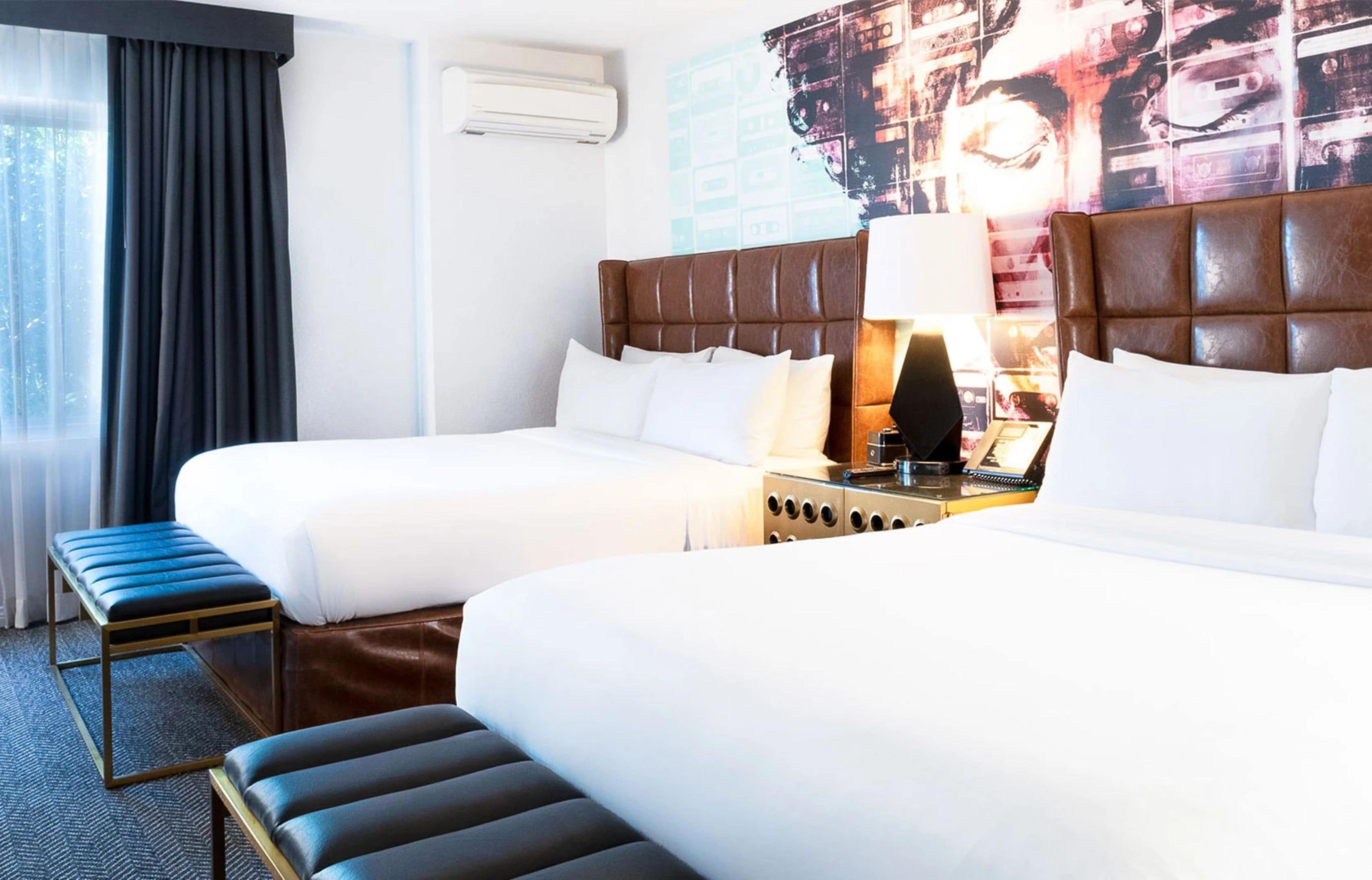 A hotel room with two beds, a bench, a nightstand, and a wall-mounted air conditioner.