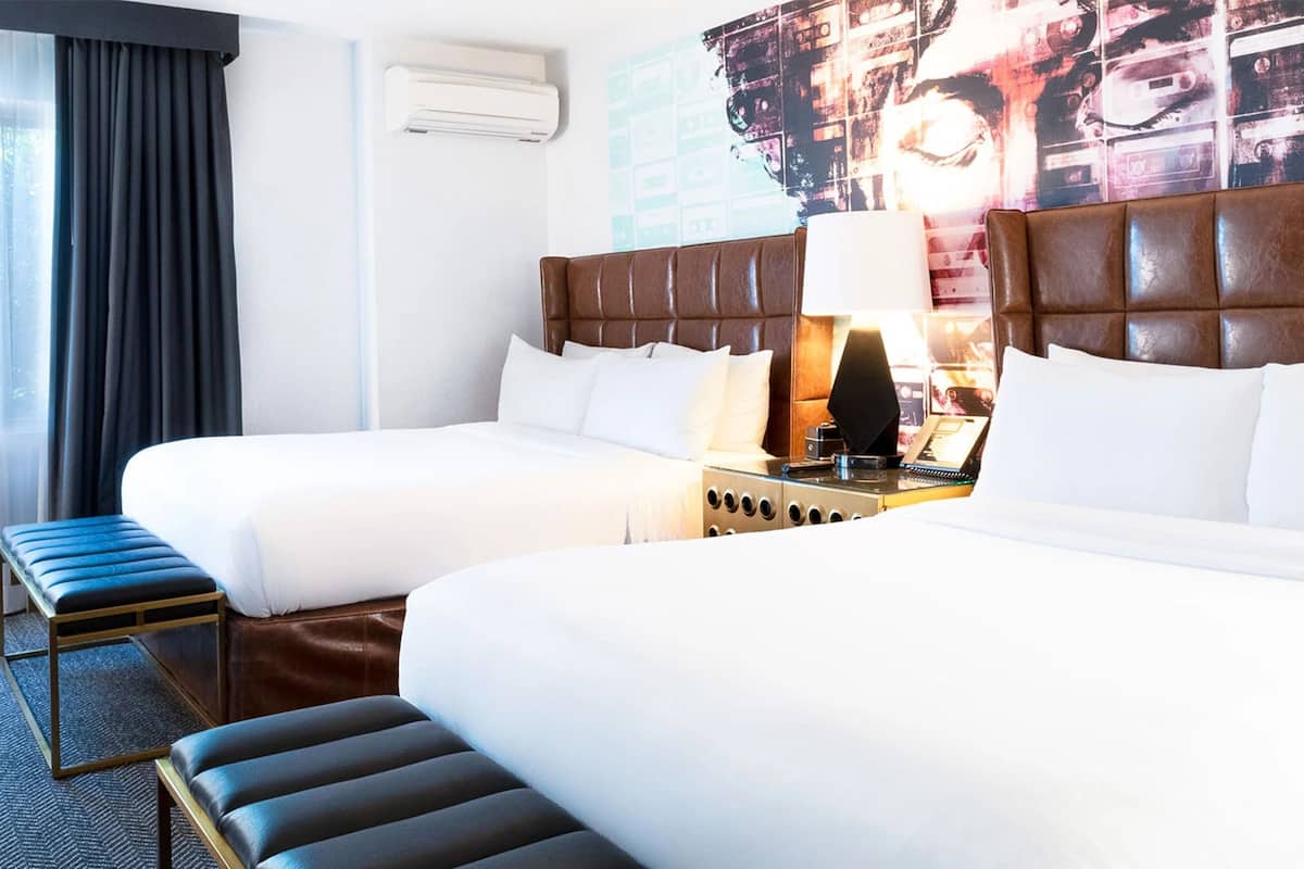 A hotel room with two beds, a bench, a nightstand, and a wall-mounted air conditioner.