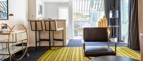 A hotel room with a dining area, a sofa, a table, a cart, and a view of the outside.