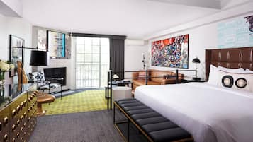 Une chambre d’hôtel avec un grand lit, un bureau, une chaise, un canapé, une télévision et un tableau au mur.