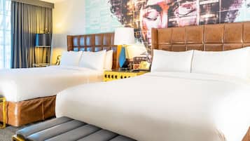 Habitación de hotel con dos camas, un mural grande en la pared, una mesita de noche con lámpara y una ventana con cortinas.