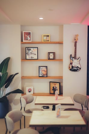 A room with a wooden shelf displaying framed pictures, a guitar, and a table with chairs.
