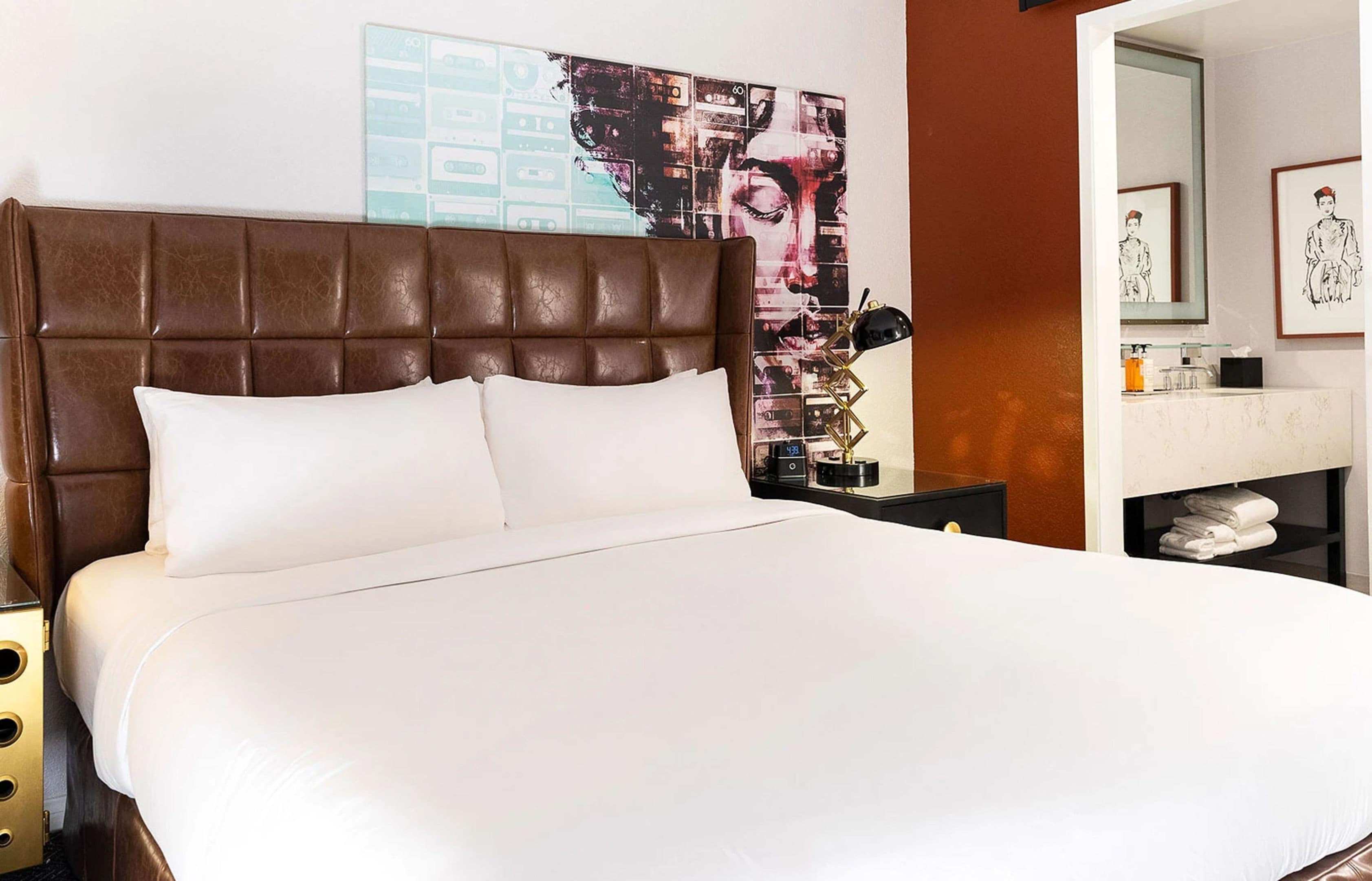 A hotel room with a large bed, a headboard, a nightstand, a mirror, and a wall with artwork.
