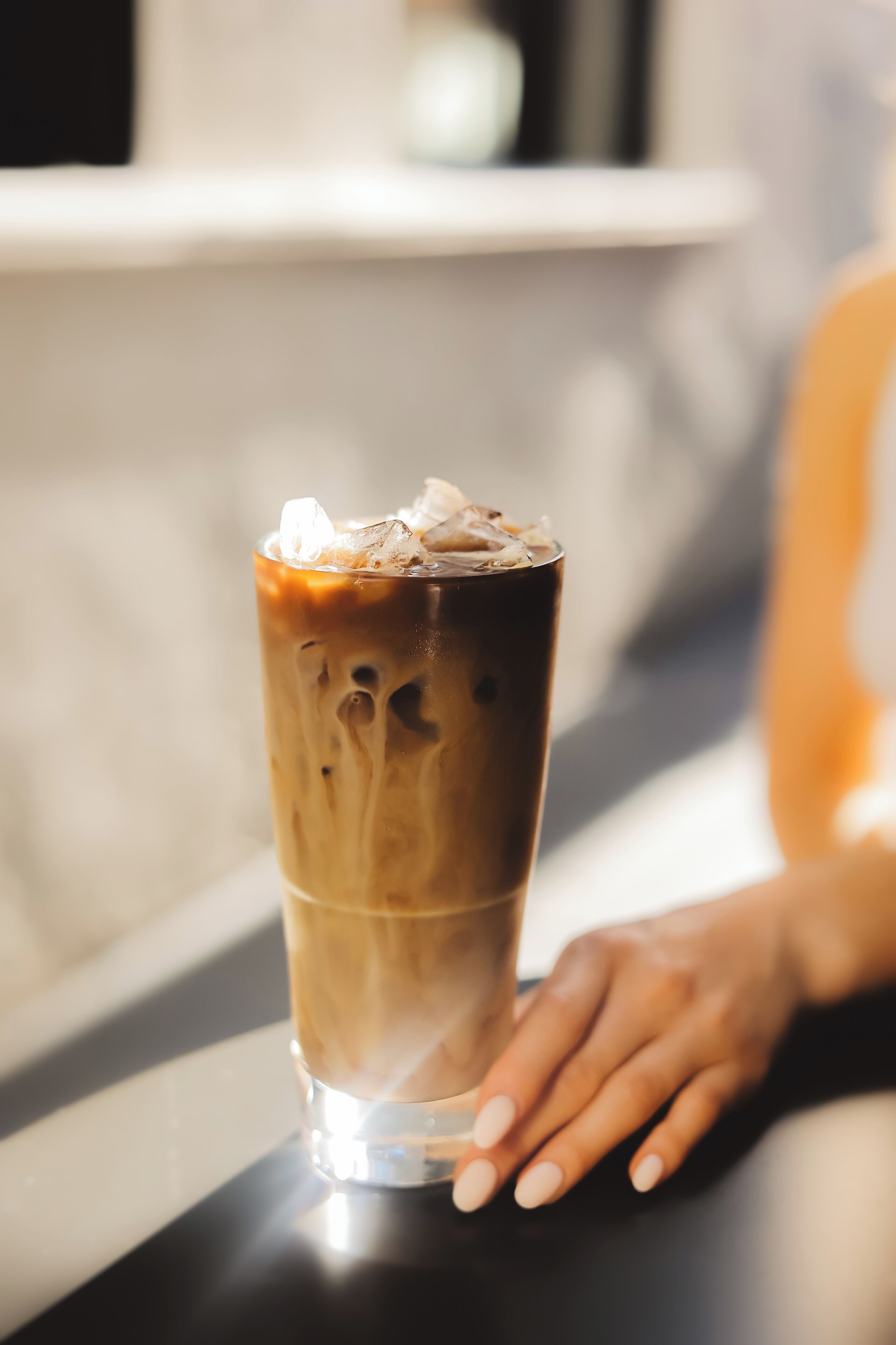 Un vaso alto de café helado con una mano apoyada sobre la mesa.