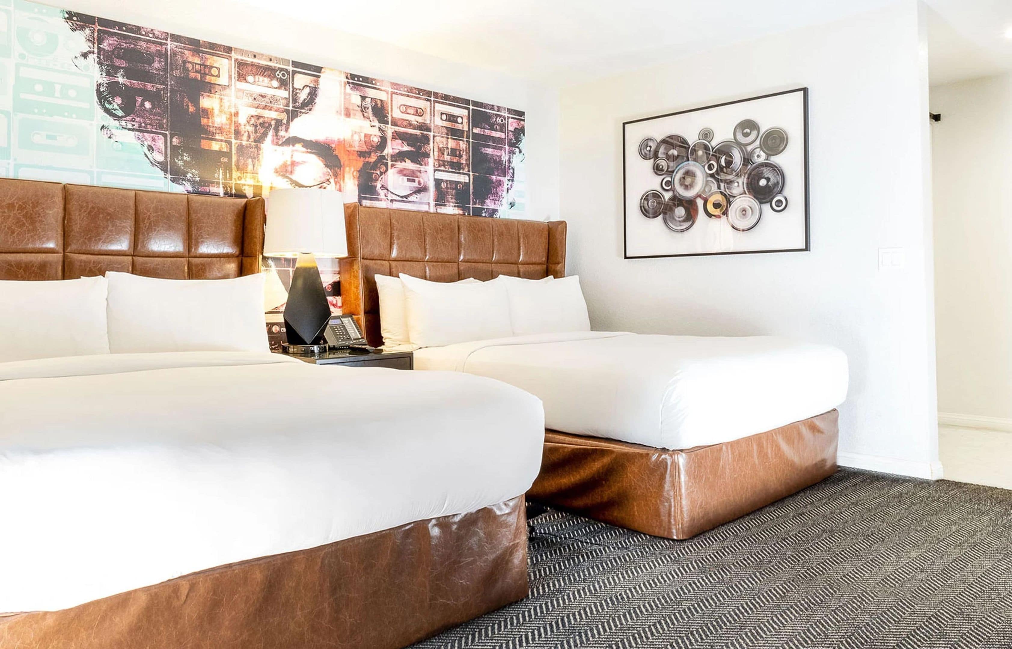 A hotel room with two beds, a headboard, a lamp, a wall art piece, and a carpet.