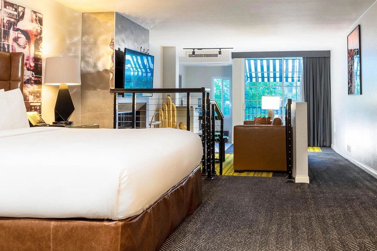 Habitación de hotel con una cama grande, un escritorio, una silla, un televisor y vistas al exterior.