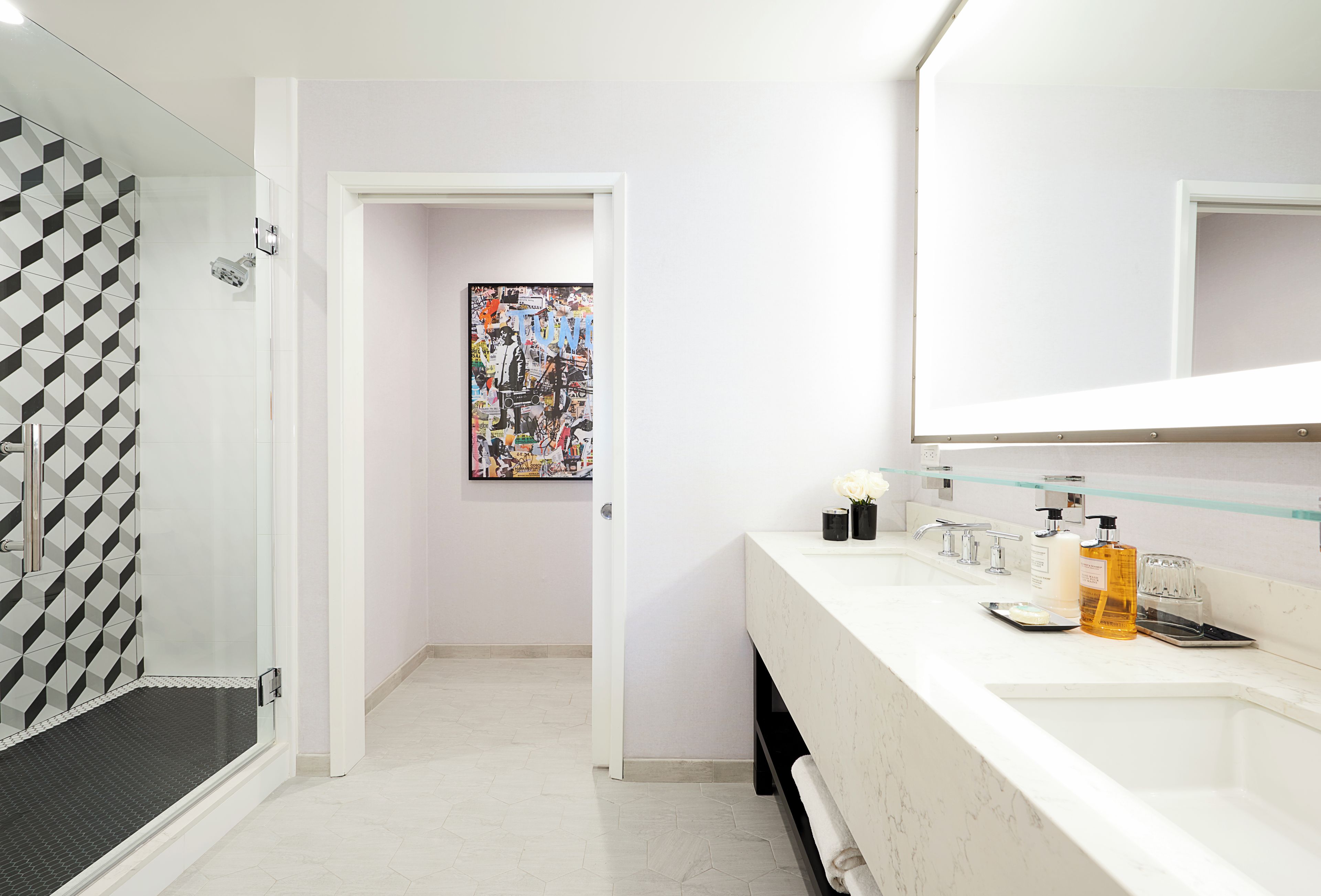 Une salle de bain moderne avec une douche, un lavabo équipé de produits de toilette et une œuvre d’art colorée accrochée au mur.