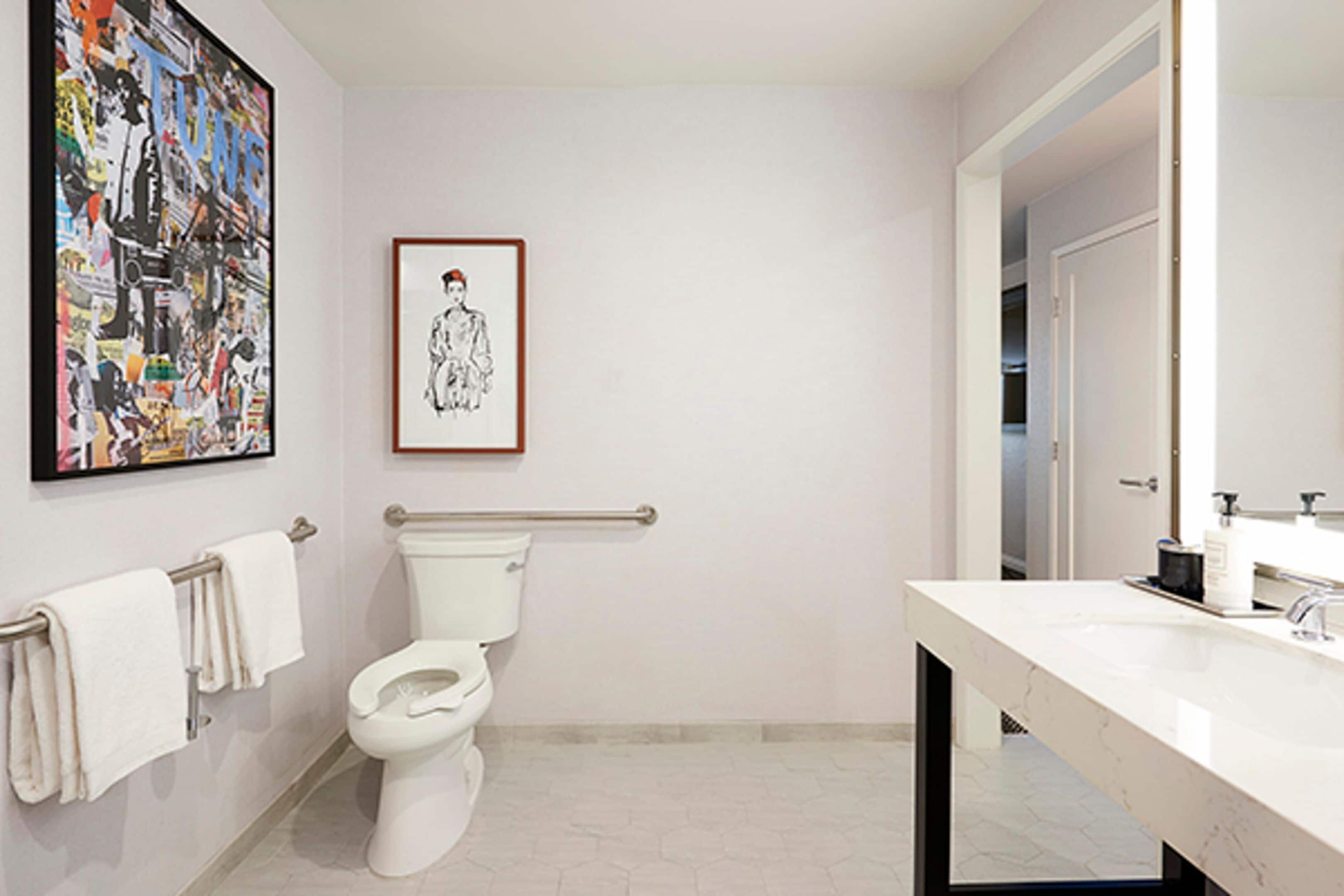 Un bagno con il water, un corrimano, un lavandino, uno specchio e un quadro appeso al muro.