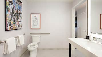 Baño con inodoro, barra de apoyo, lavamanos y espejo. Hay un cuadro en la pared.