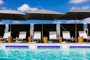 A swimming pool area with lounge chairs and umbrellas.
