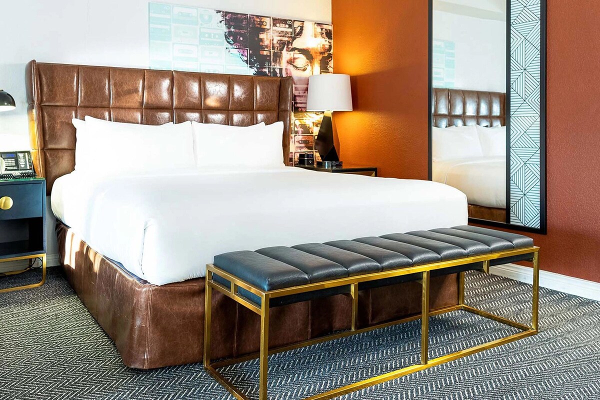 Una habitación de hotel con una cama grande, un banco, una mesita de noche, una lámpara y una pared con un diseño geométrico.