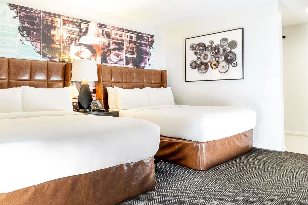 Een hotelkamer met twee bedden, een hoofdeinde, een lamp, een kunstwerk aan de muur en een vloerkleed.