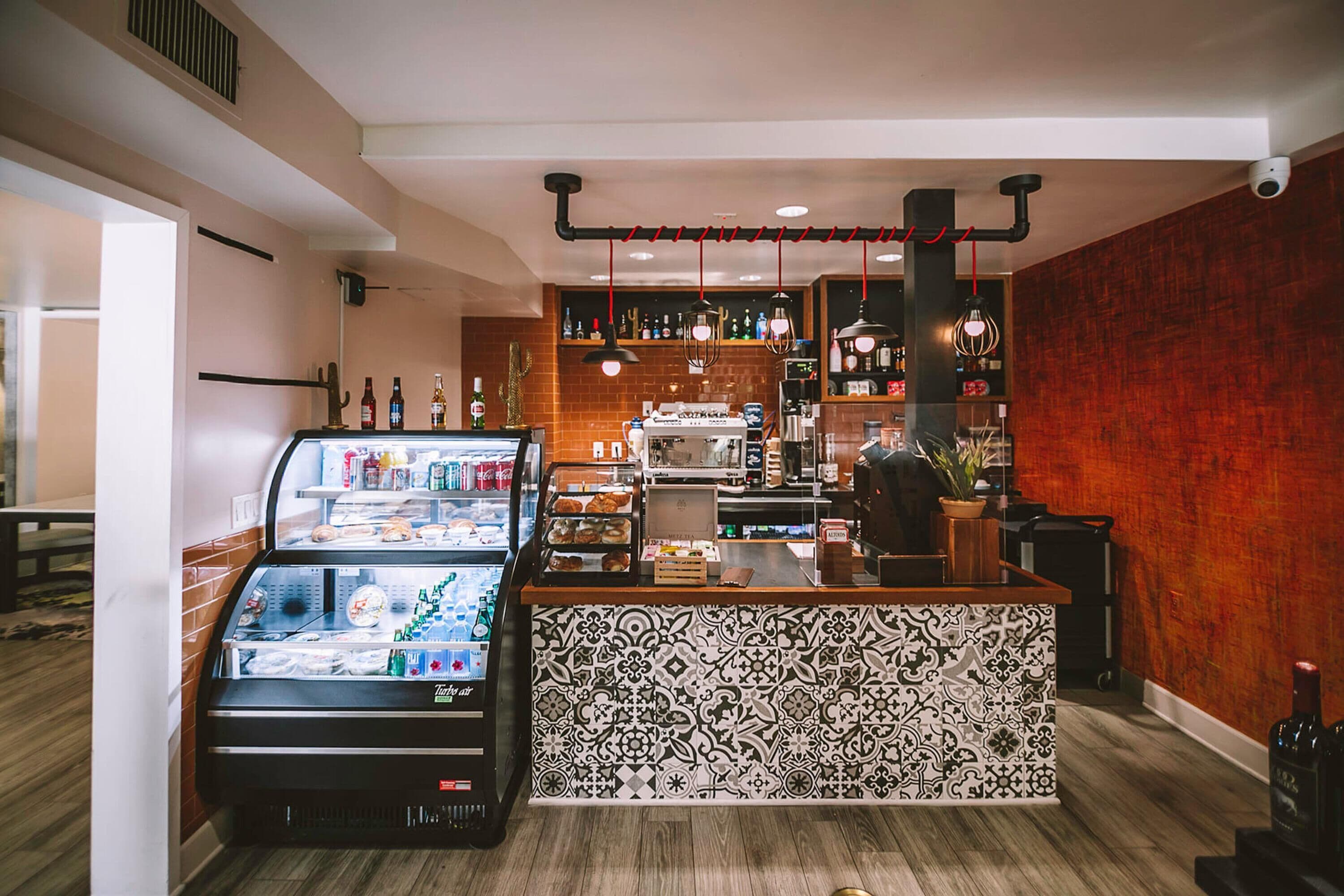A café with a refrigerated display case, a patterned counter, and shelves stocked with beverages.