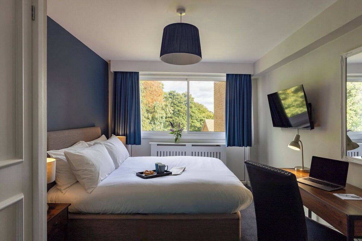 Une chambre d’hôtel avec un lit, un bureau avec un ordinateur portable, un téléviseur fixé au mur et une fenêtre avec des rideaux.