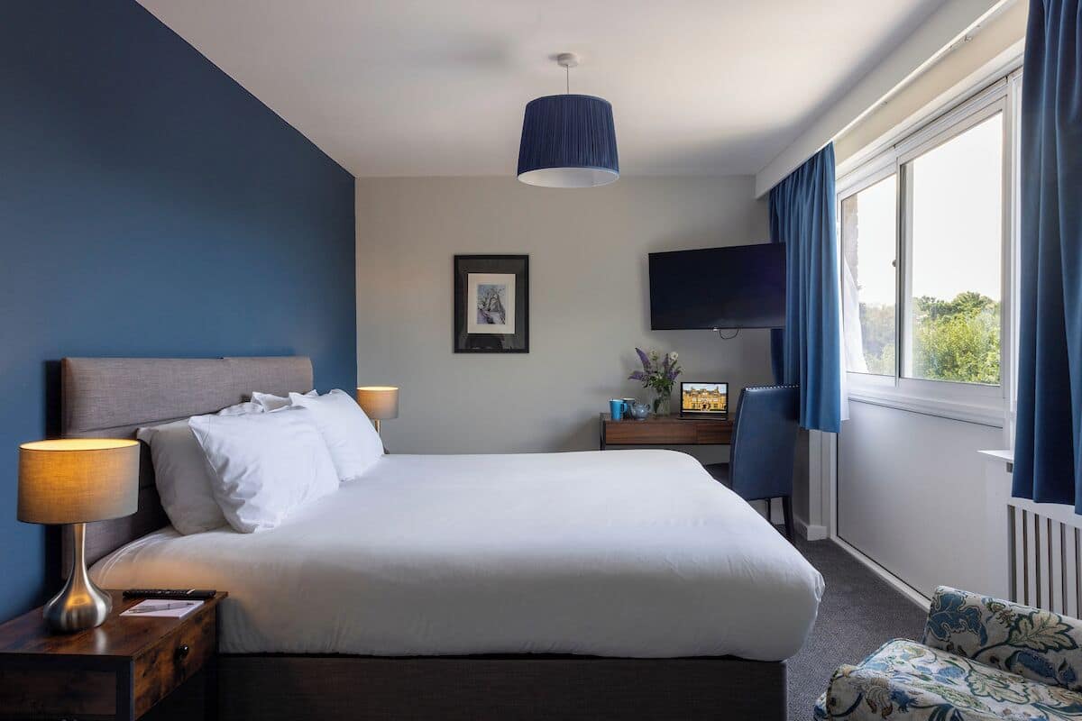 Une chambre d’hôtel dotée d’un grand lit, d’un téléviseur à écran plat, d’un bureau avec une lampe et offrant une vue sur l’extérieur par une fenêtre.