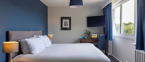Habitación de hotel con una cama grande, un televisor de pantalla plana, un escritorio con lámpara y vistas al exterior a través de una ventana.