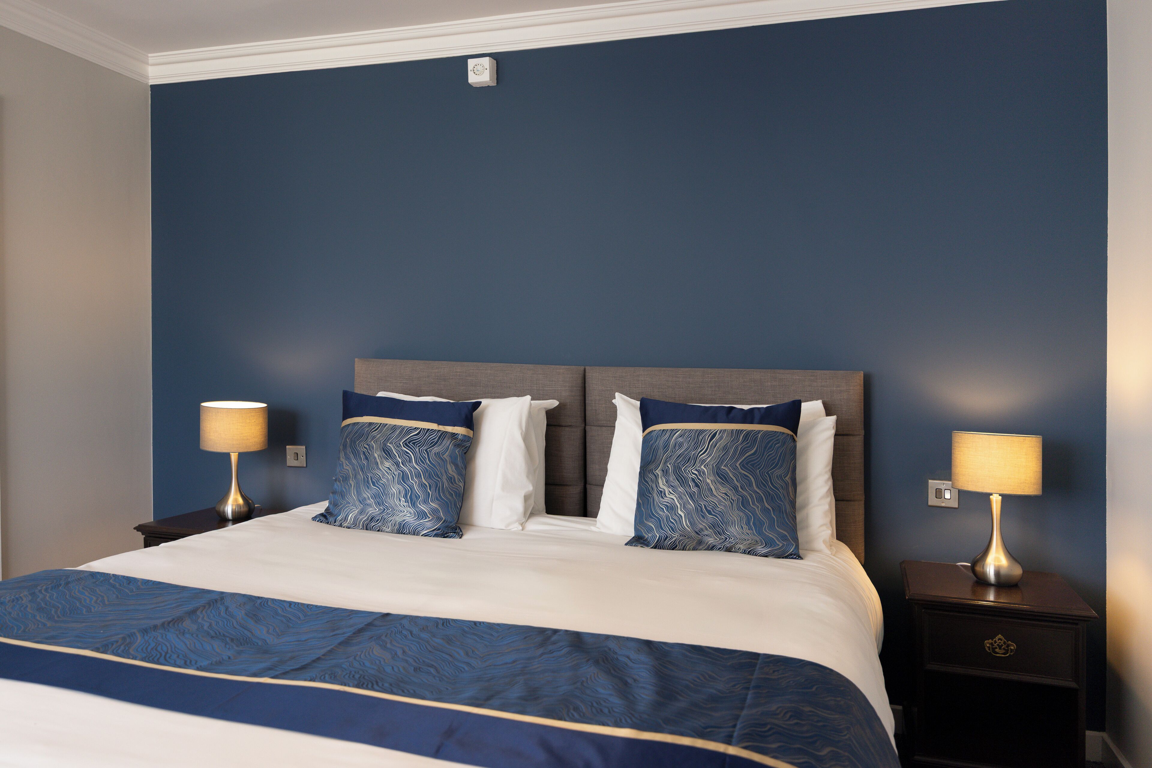 A hotel room with a large bed, two bedside tables, and a wall-mounted light fixture.