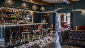 Un espace bar comprenant un comptoir, des tabourets et une variété de bouteilles. Il y a également un coin salon avec un canapé en cuir et des fauteuils.